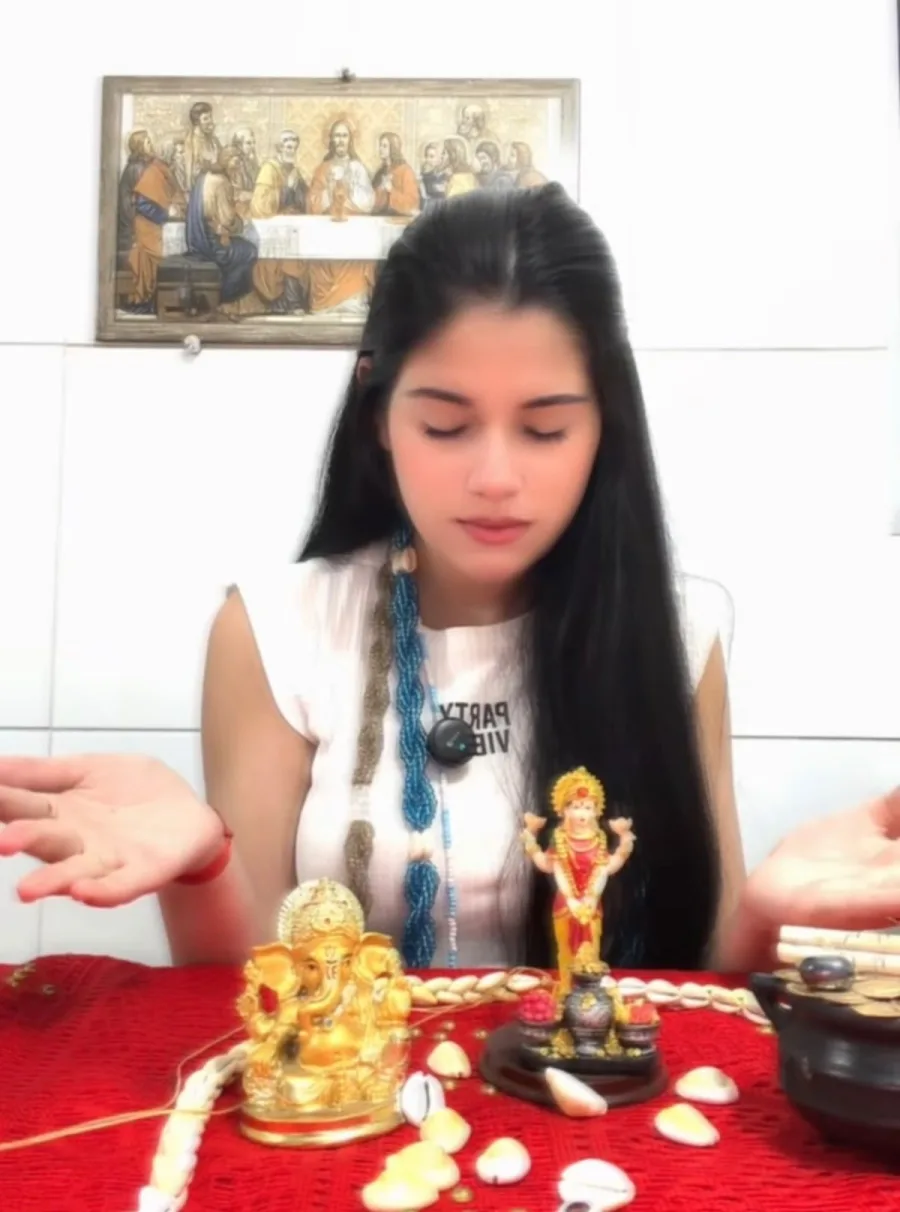 Melissa de olhos fechados diante de uma mesa vermelha com búzios e uma imagem dourada de Ganesha