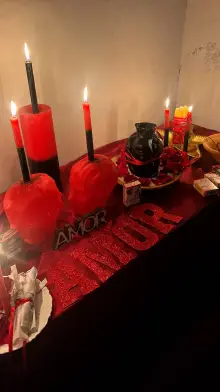 Mesa de ritual com velas vermelhas e pretas, velas em forma de cabeça, rosas e a palavra AMOR